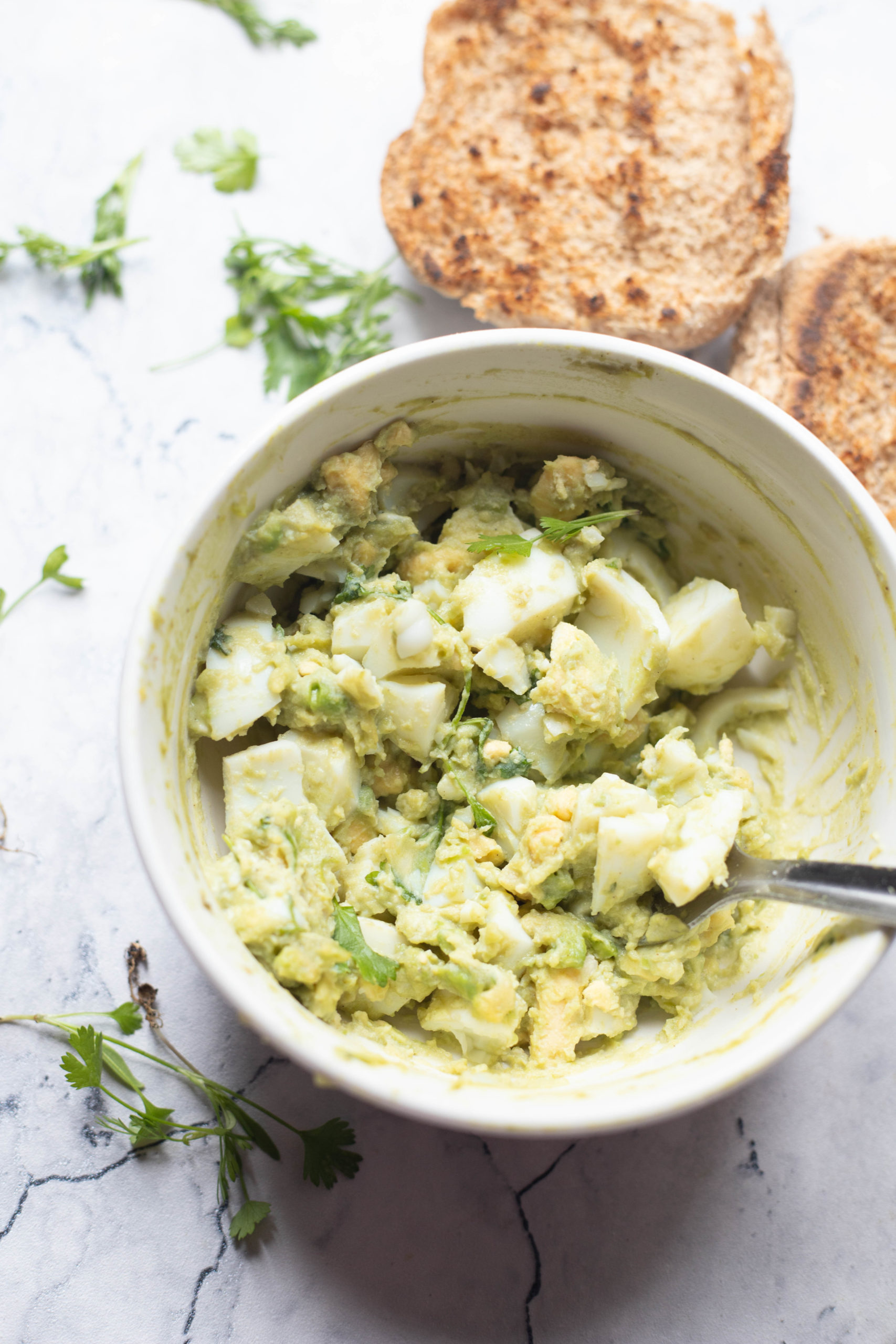 Bowl of avocado egg salad with brown bread on side