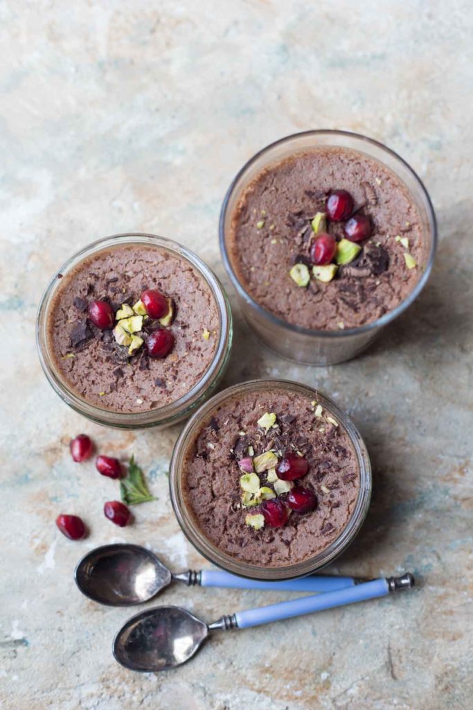 3 serves of vegan chocolate mousse with aquafaba garnished with pomegranate seeds and pistachios along with 2 spoons