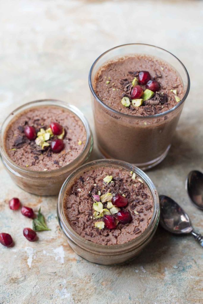 3 serves of vegan chocolate mousse with aquafaba garnished with pomegranate seeds and pistachios with 2 spoons aside 