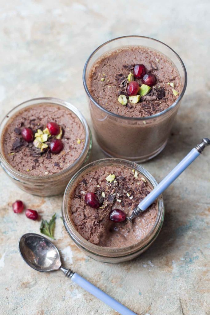 3 serves of vegan chocolate mousse with aquafaba garnished with pomegranate seeds and pistachios along with 2 spoons