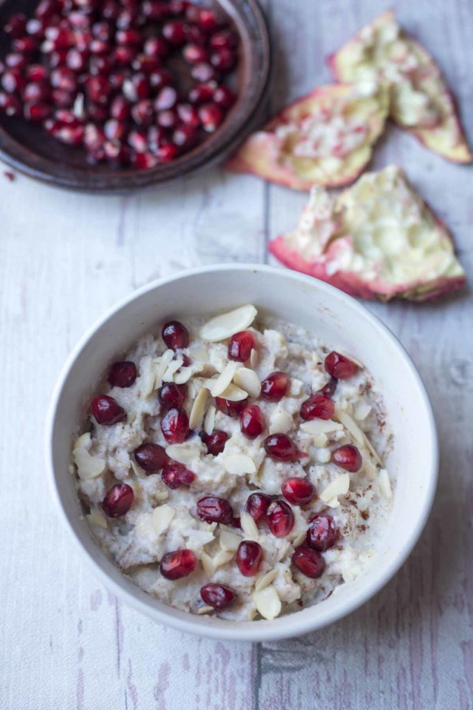 millet porridge served with fresh fruit and almond flakes in a bowl with a plate of pomegranate seeds .