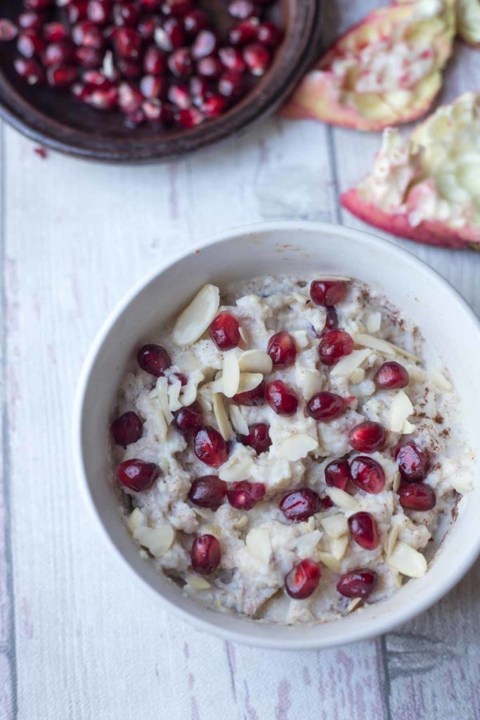 millet porridge served with fresh fruit and almond flakes in a bowl with a plate of pomegranate seeds .