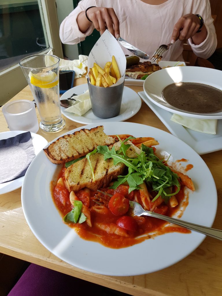 a plate full of pasta, skinny fries, a glass of water, soup served in white deep plate and a girl eating