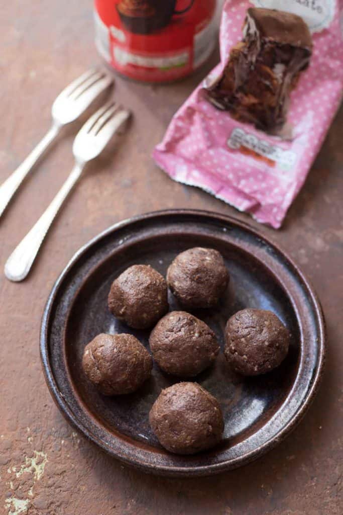 6 Avocado chocolate protein balls served on a brown plate with 2 forks, a pack of chocolate bar and cocoa powder