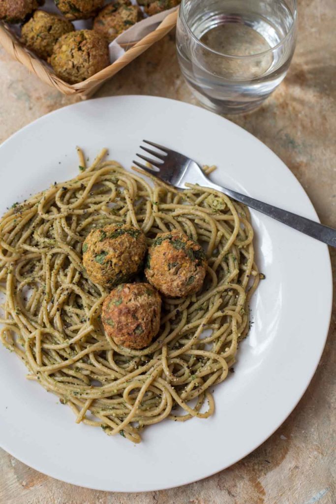 vegan spinach lentil meatballs served on pesto pasta with a glass of water