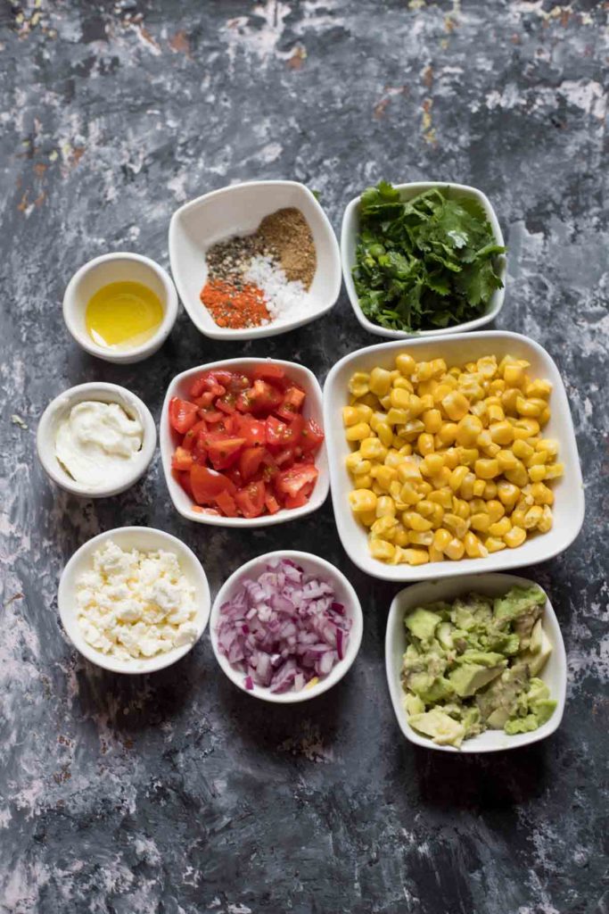 Ingredients for mexican street corn salad, sweet corn,avocados,red onions,feta cheese tomatoes olive oil, spices coriander,quark 