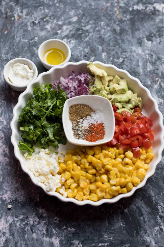 Mexican street corn salad served in a white plate with silver spoon