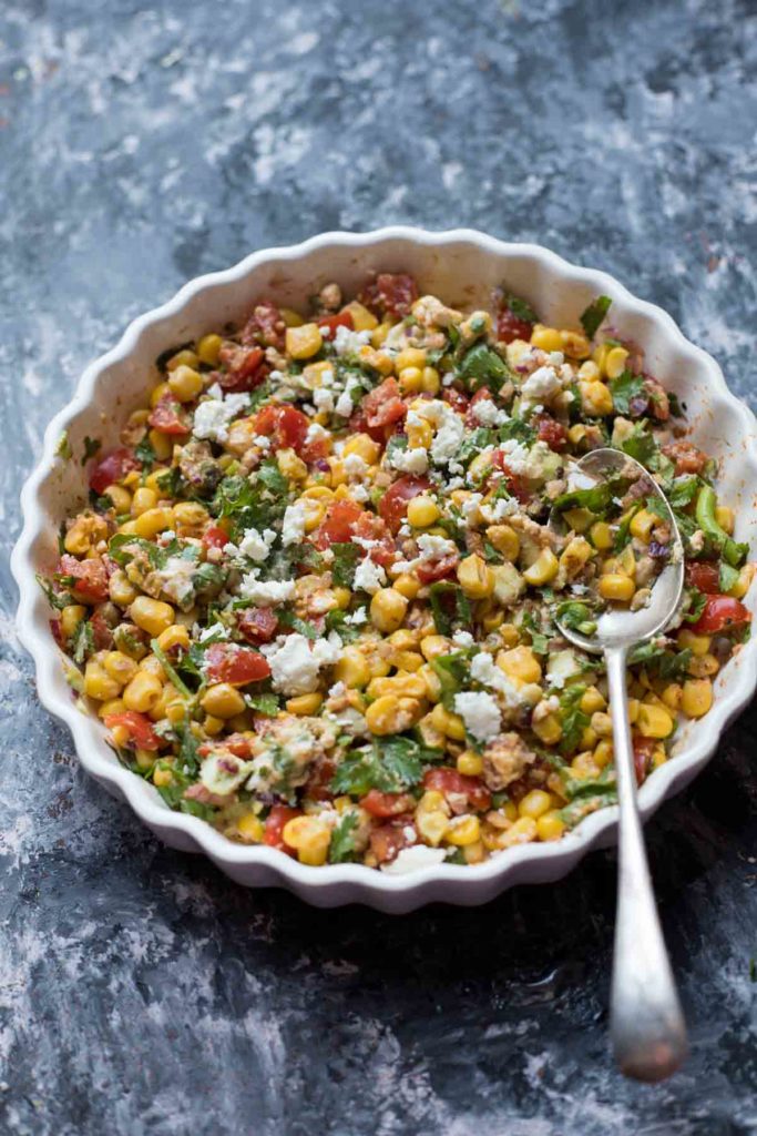 Mexican street corn salad served in a white plate with silver spoon