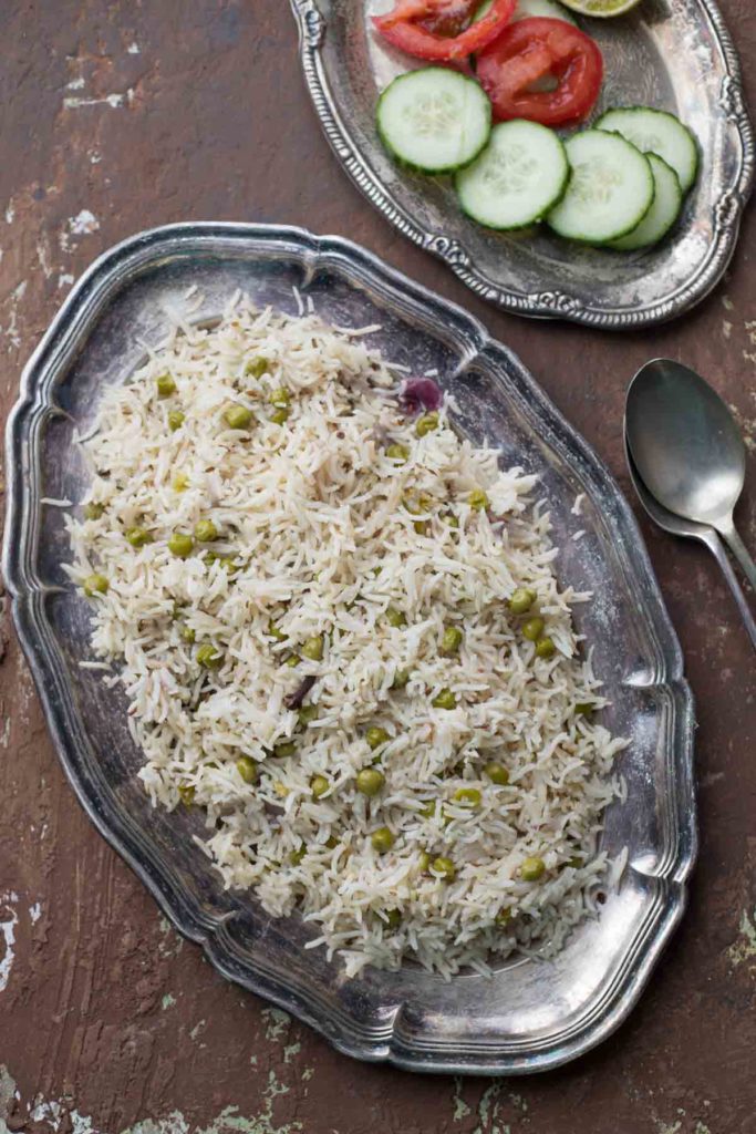 Instant Pot Green peas pulao served on a silver plate and onion, tomato salad