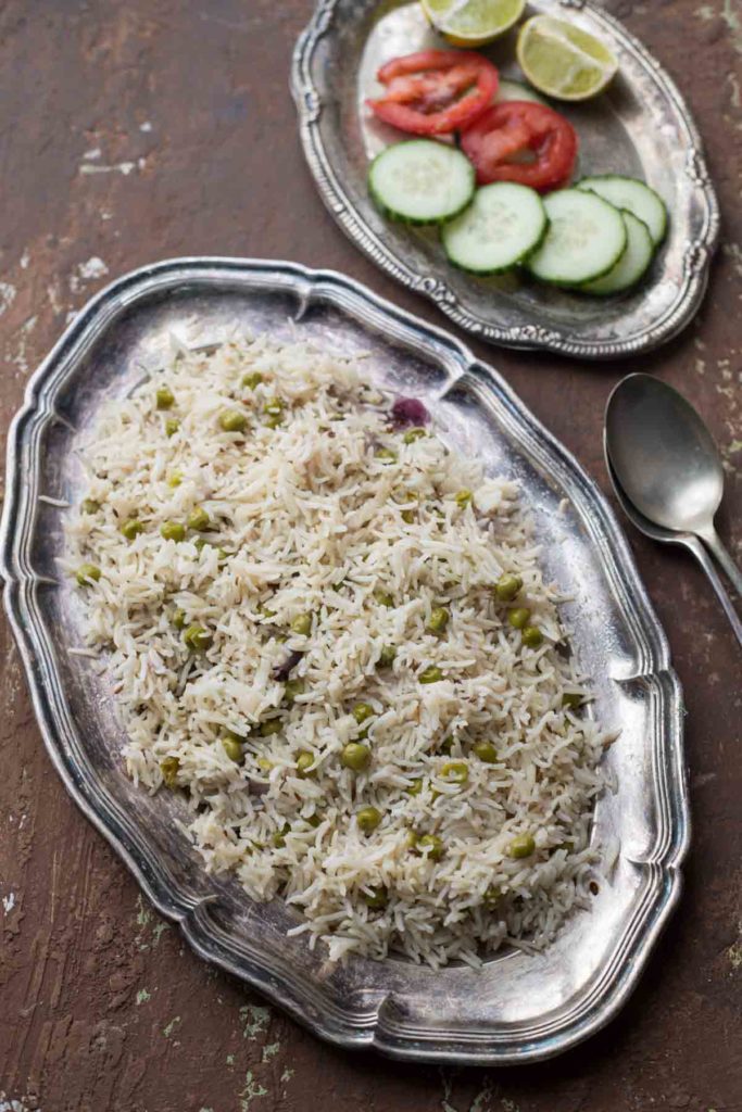 Instant Pot Green peas pulao served on a silver plate and onion, tomato salad