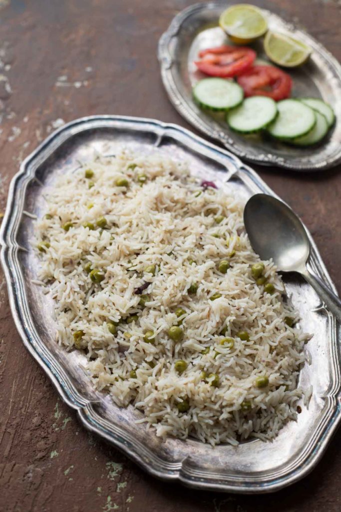 Instant Pot Green peas pulao served on a silver plate and onion, tomato salad