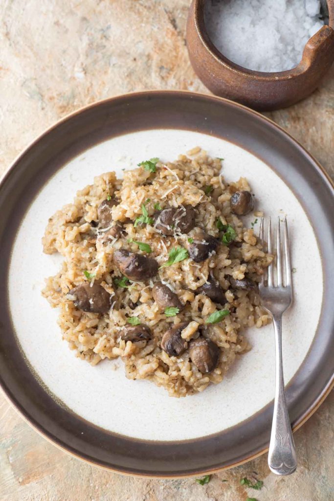 mushroom risotto served on a white plate along with a silver fork and salt in the bacground