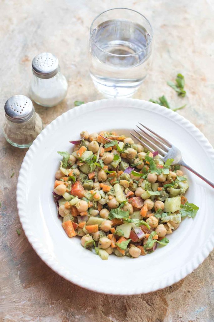 vegan pesto chickpea salad served in a white plate with salt, pepper and a glass of water on the background