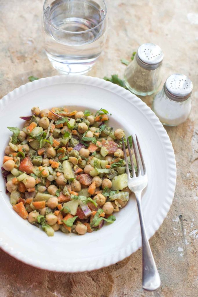 vegan pesto chickpea salad on a white plate with salt, pepper and a glass of water in the background