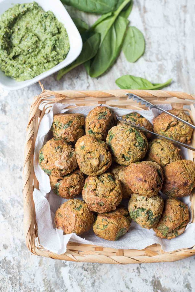 vegan spinach lentil meatballs with basil pesto and spinach leaves in the background