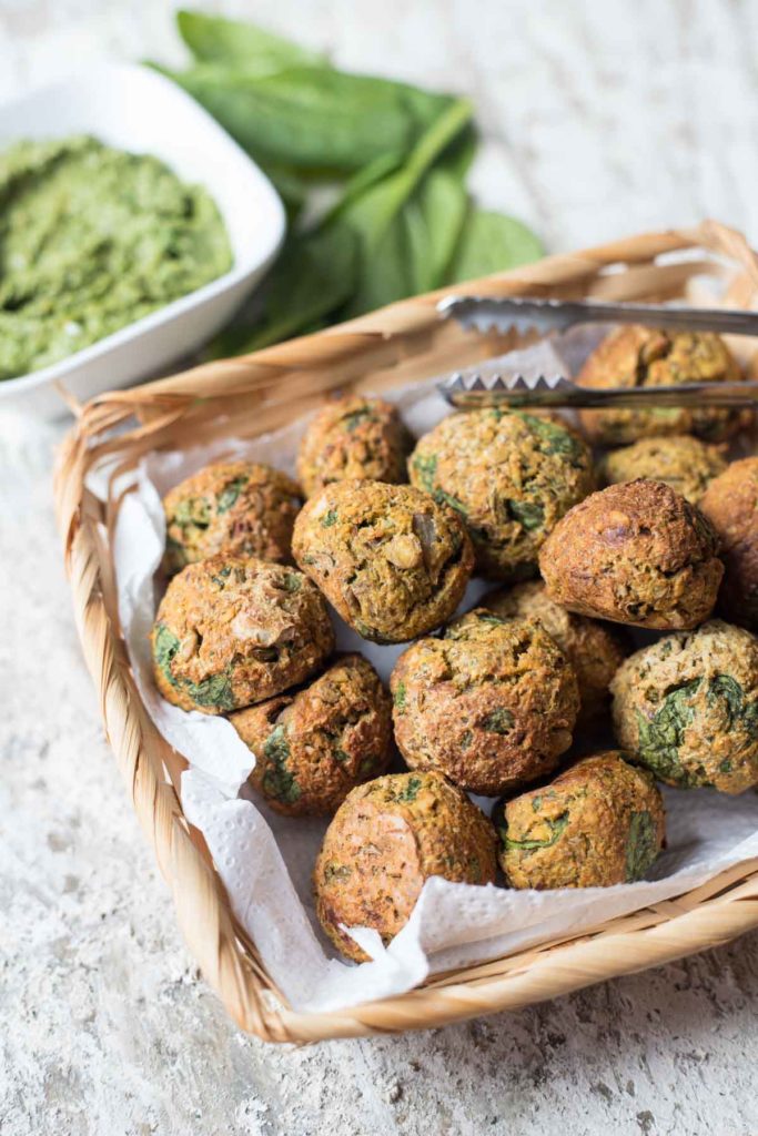 vegan spinach lentil meatballs with a serving tong and pesto in the back