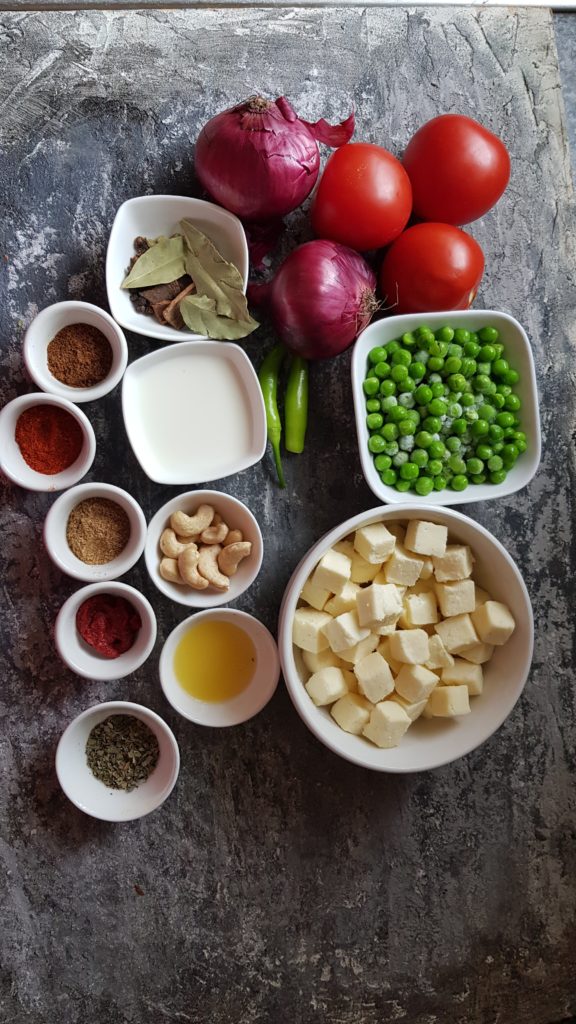 Ingredients to make instant pot matar paneer, onions, tomatoes, cashews, milk, chilli, whole spices, butter, spice powders.