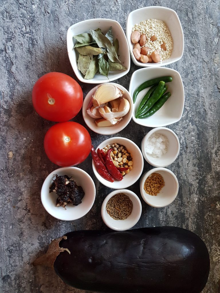 Ingredients for making vankaya pachadi, tomatoes, eggplant, garlic cloves, green chillis, curry leaves,urad dal,channa dal, mustard seeds, dried red chillis,tamarind