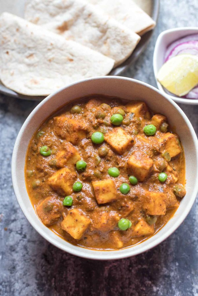 Matar Paneer curry served in a bowl along with indian flat bread and onion salad