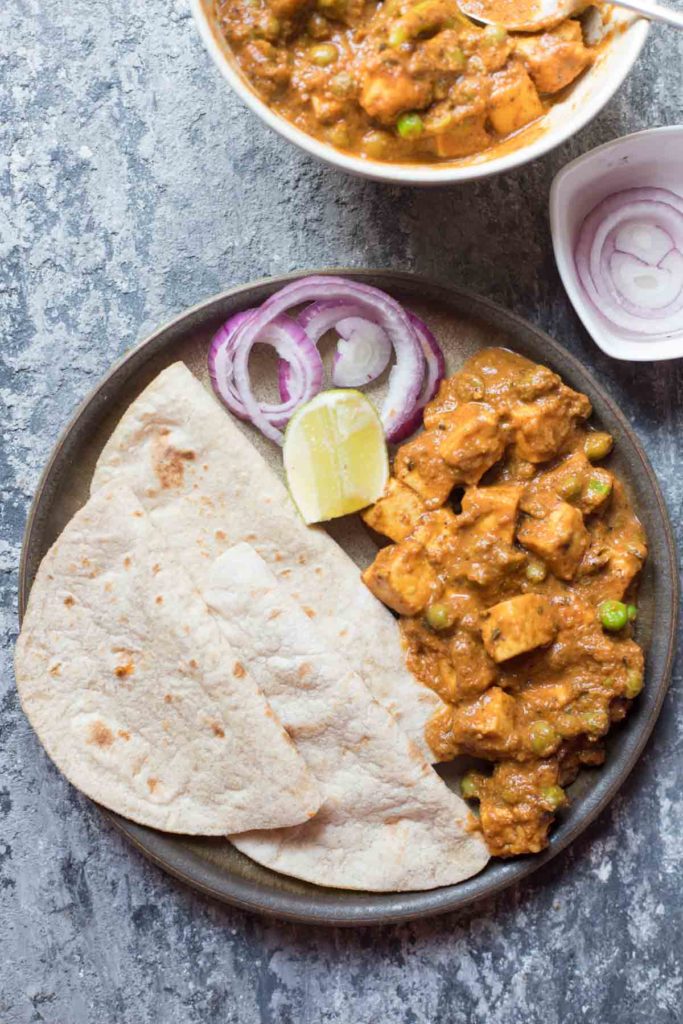 Matar Paneer curry and Indian flat bread served on a plate along with onion and lemon