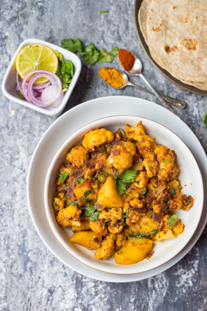 a bowl of instant pot aloo gobi and onion salad, 2 spoons of turmeric, chili and indian flat breads