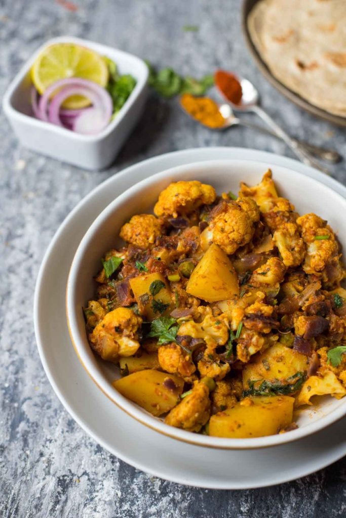 bowl of aloo gobi with rotis and onion,lemon