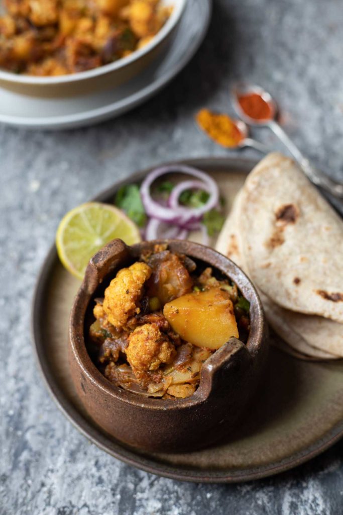 a small bowl of aloo gobi curry with chapati, onion slices and lemon wedge