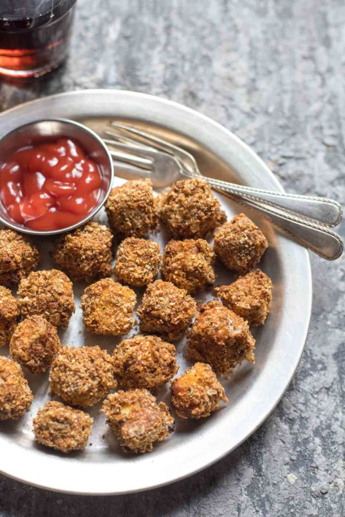 A plate of paneer popcorn , a small bowl of ketchup and 2 forks