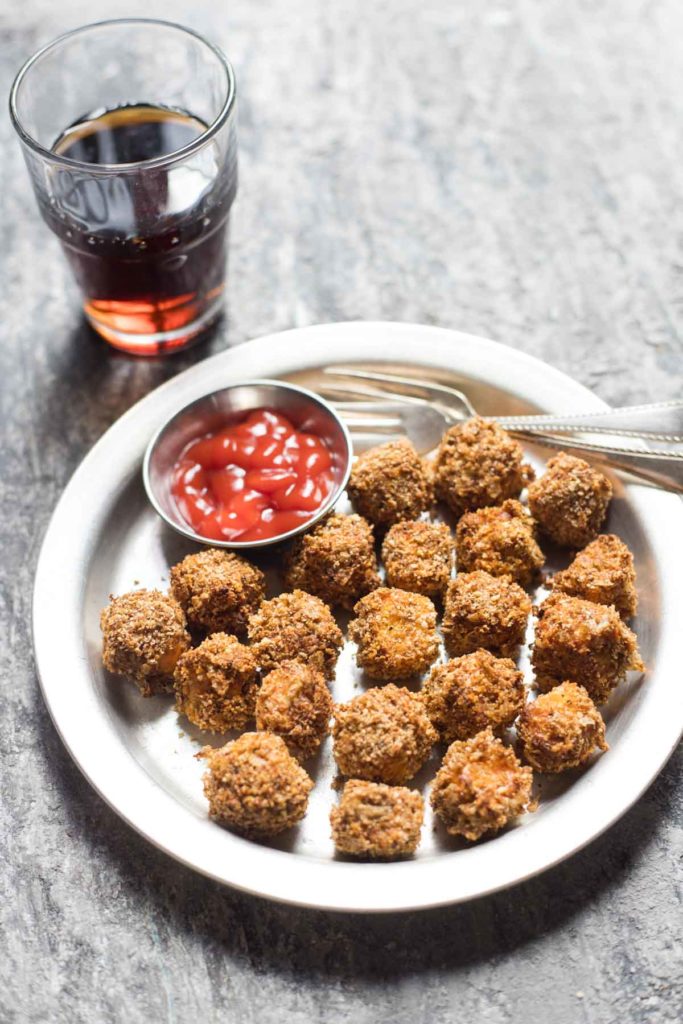 A plate of paneer popcorn served with ketchup and fork along with a glass of diet coke