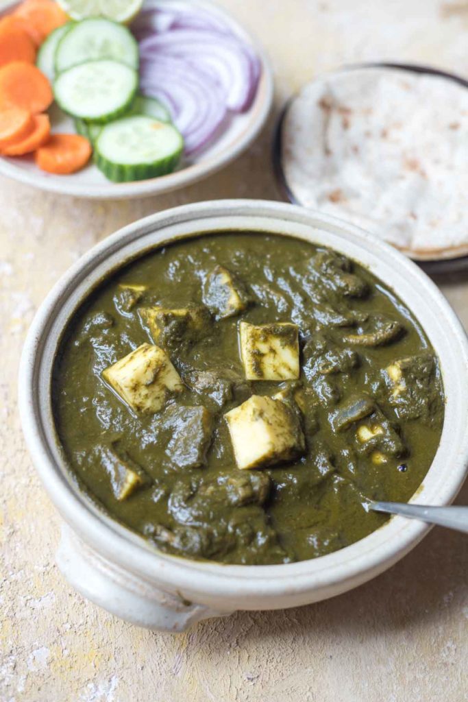 mushroom palak paneer served in a white bowl, rotis, salad