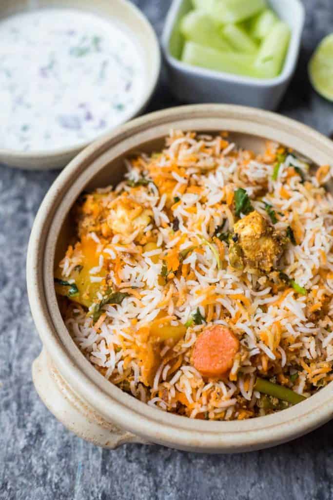 hyderabadi dum biryani in a clay pot , cucumber salad, raitha, lime wedge, spoons