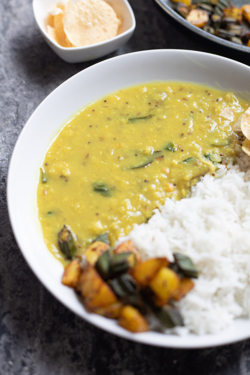 raw mango dal served with rice and stir fry in a white plate, papads in background