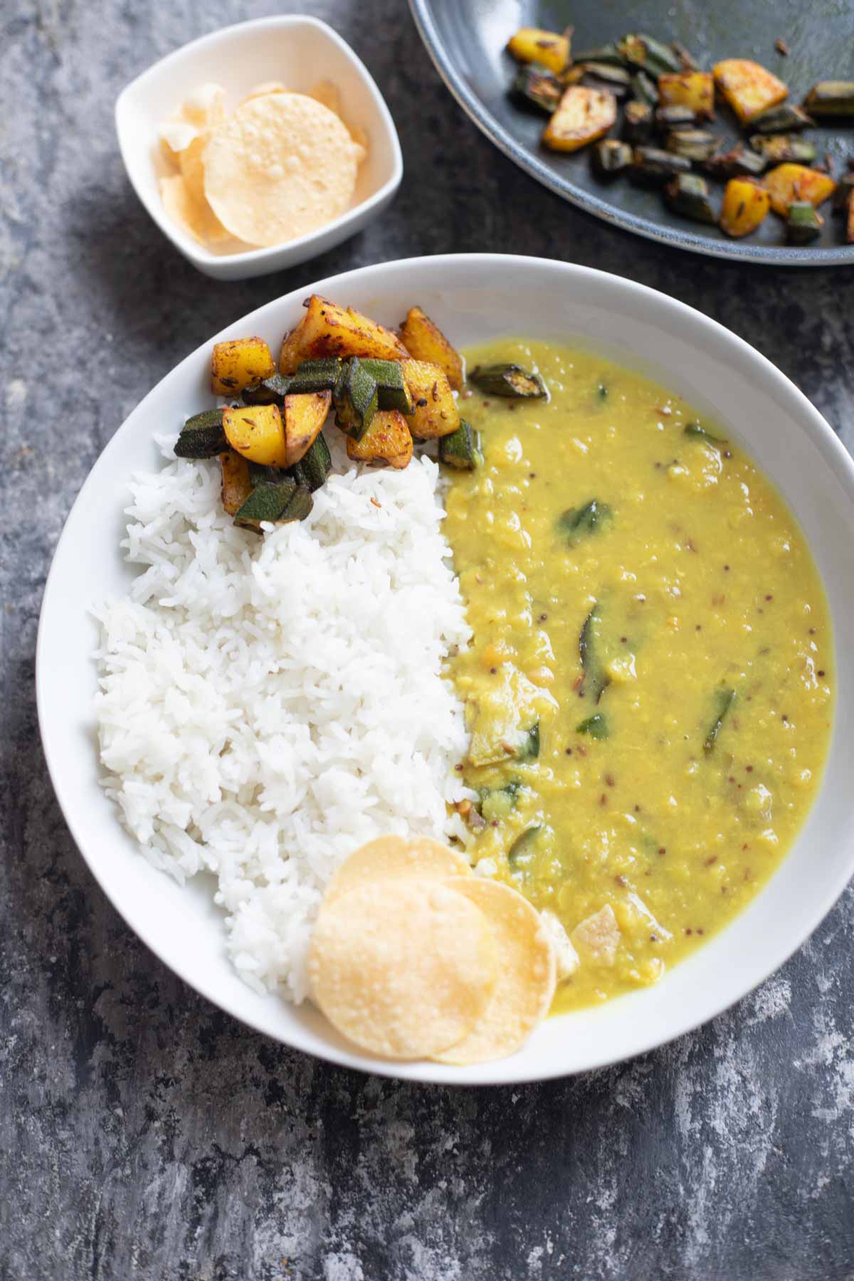 raw mango dal served with rice and stir fry in a white plate, papads in background