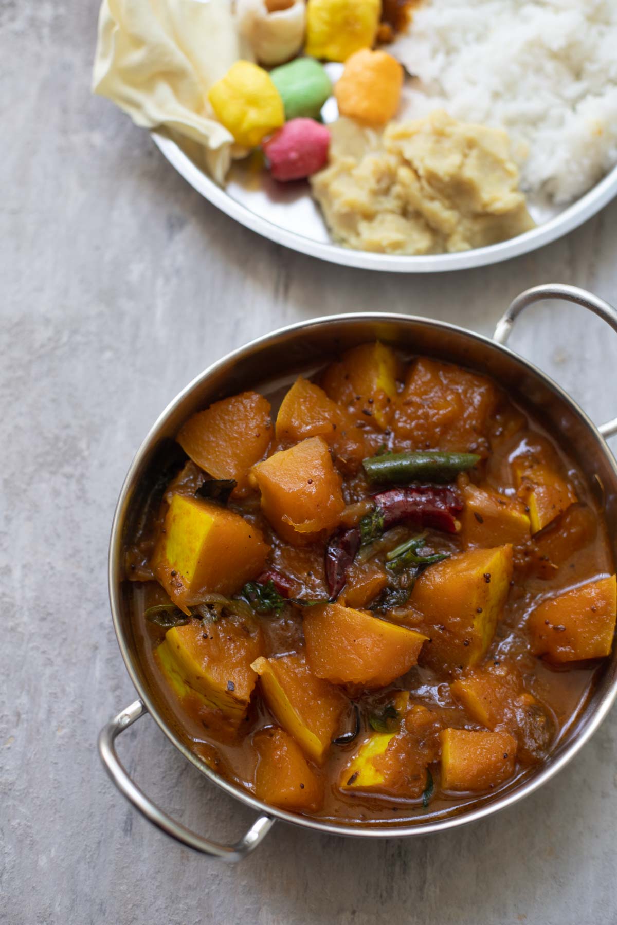 gummadikaya pulusu served in a kadai with rice and papds in background