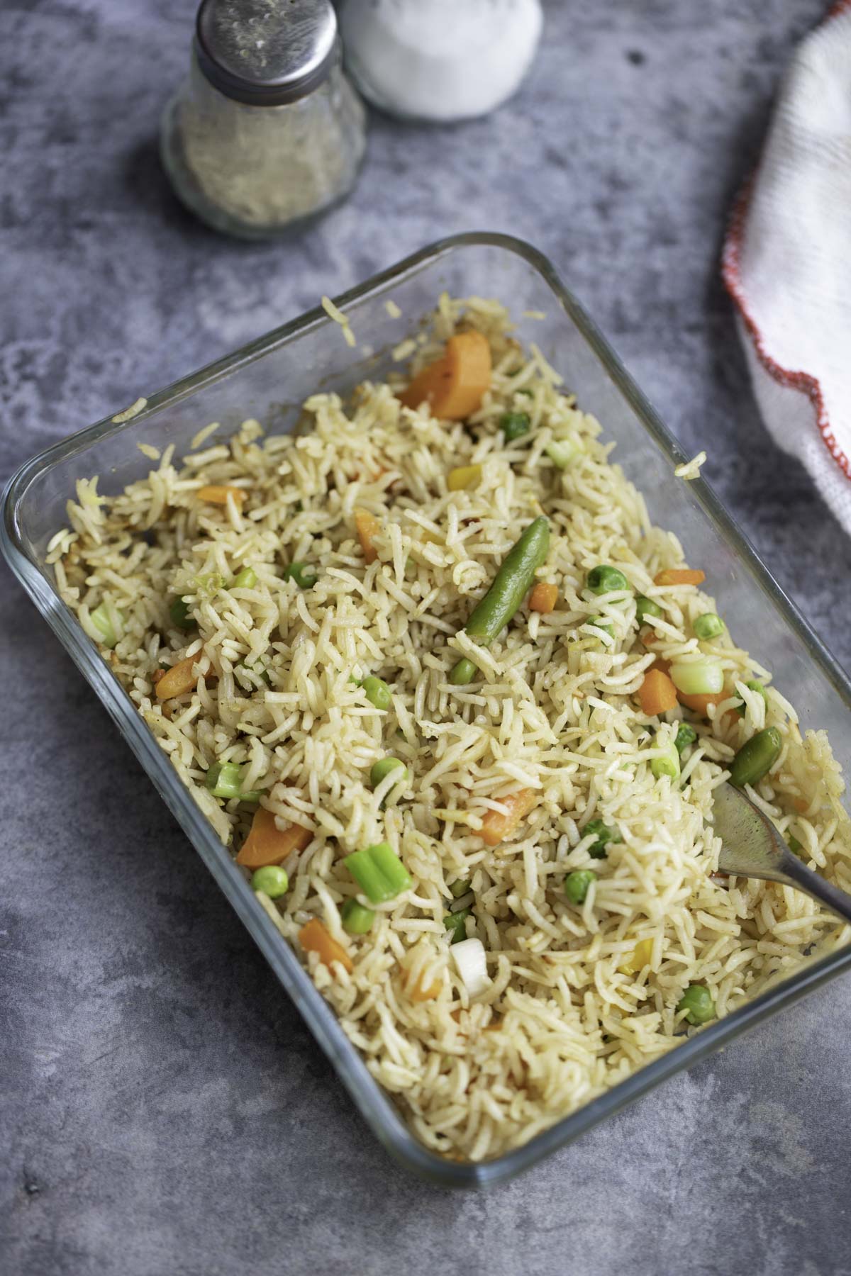 a glass container with fried rice, white napkin and salt and pepper in the background