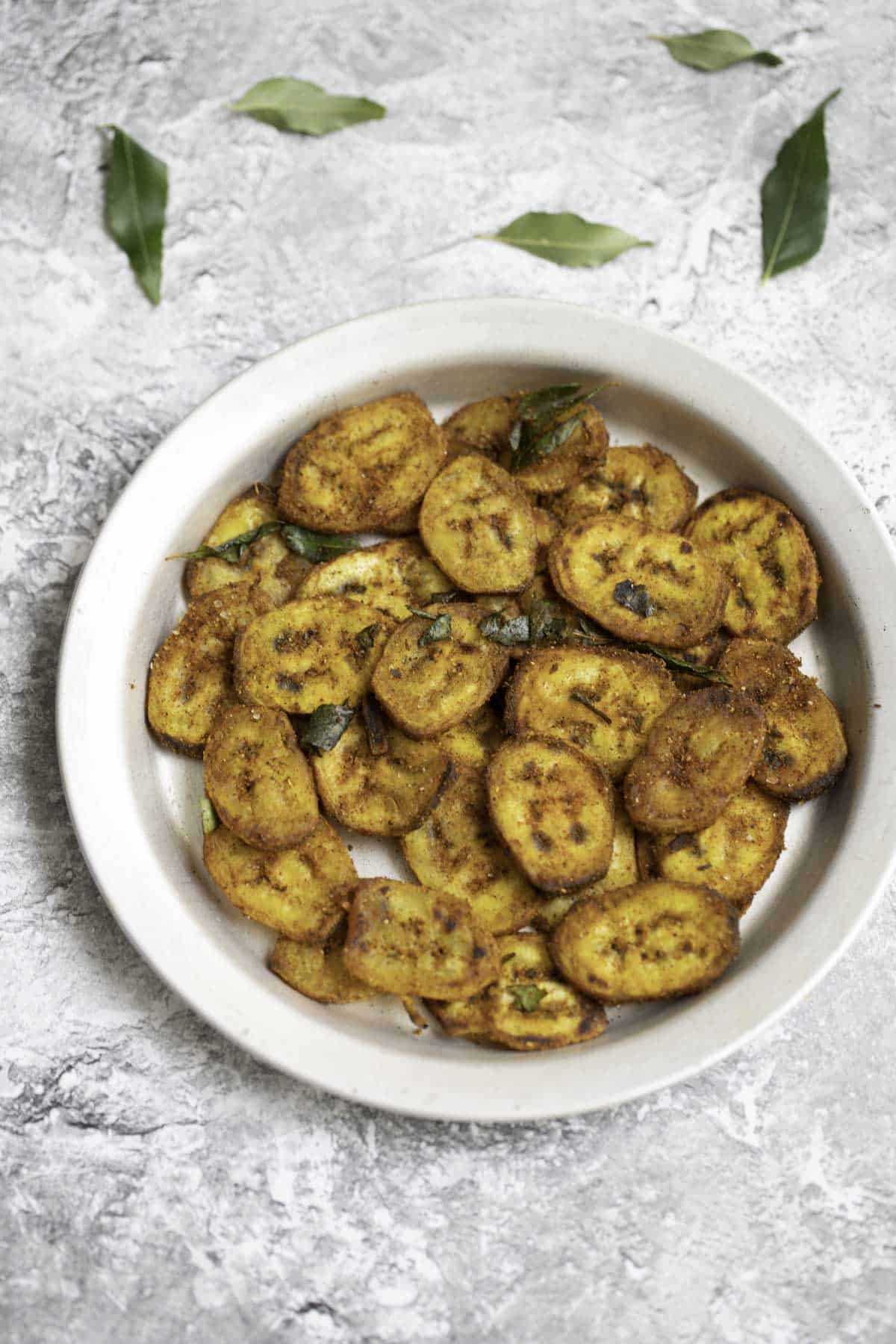 a plate of raw banana fry with curry leaves in the background for decor