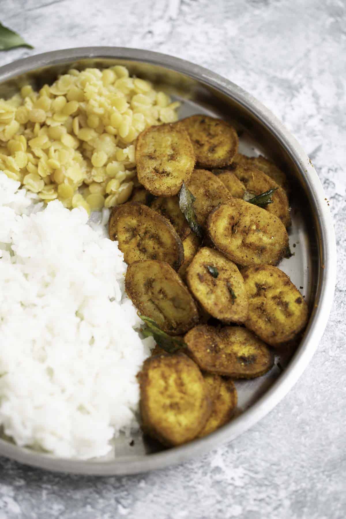 a plate of cooked white rice, dal, raw banana fry