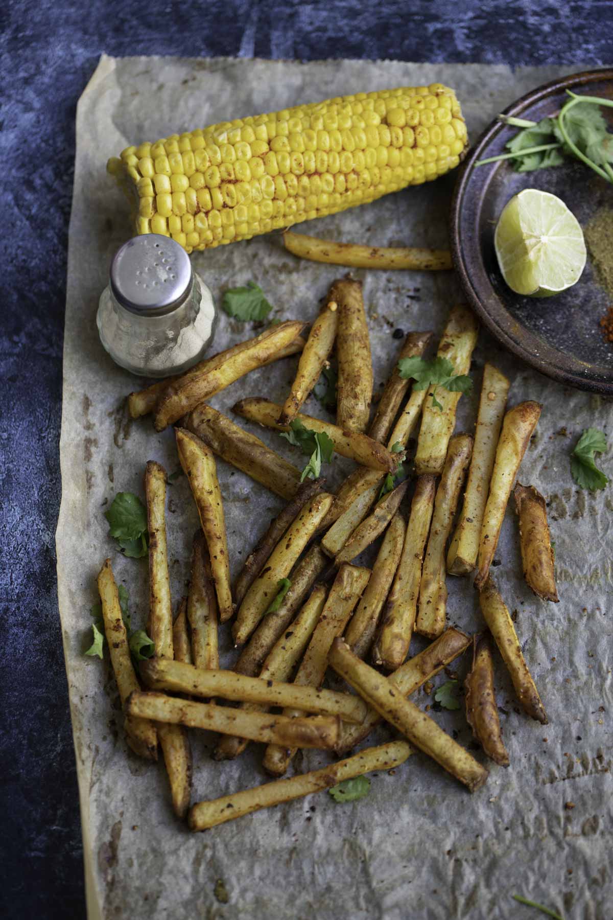 baked masala fries on a baking paper. pepper, corn on the cob and a lemon wedge in the background