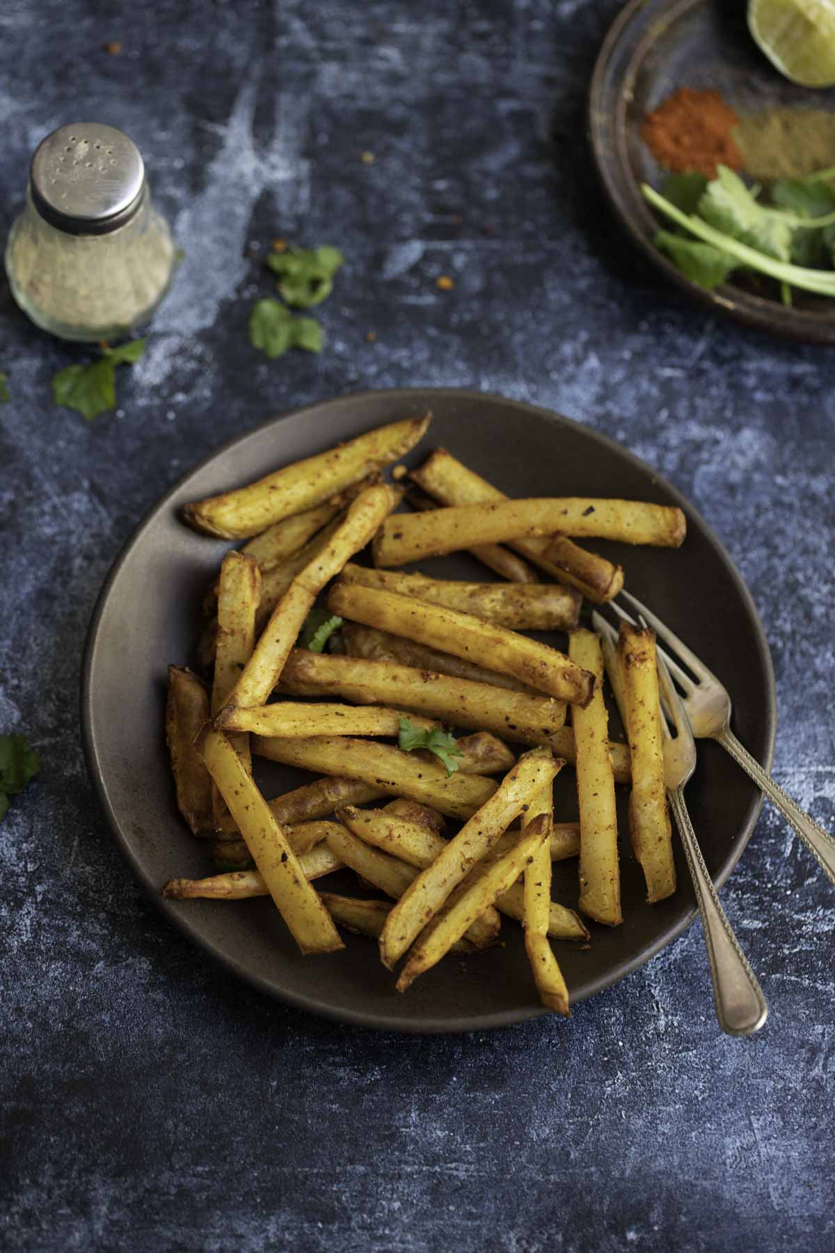 a plate of masala fries with salt and pepper to back of it