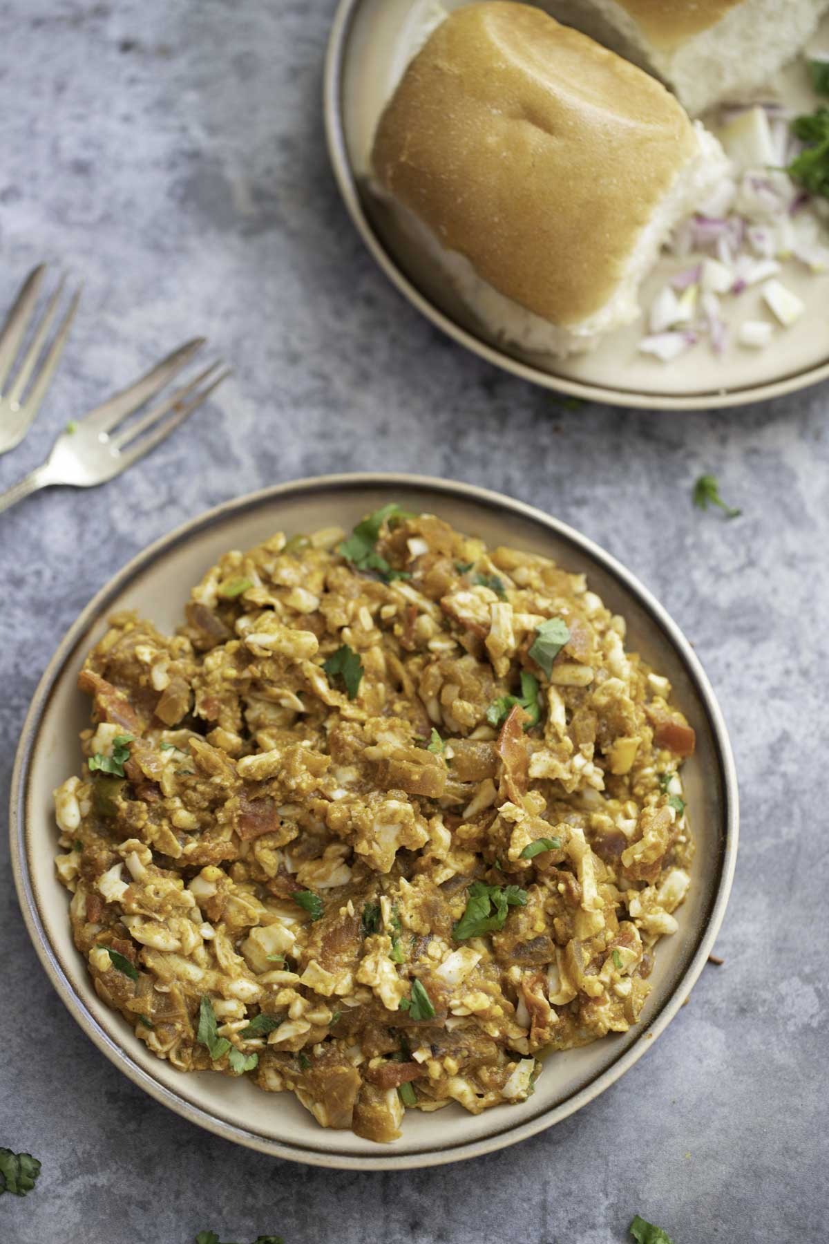 egg keema on a plate , 2 forks and a plate of pav bread ,chopped onions in the background