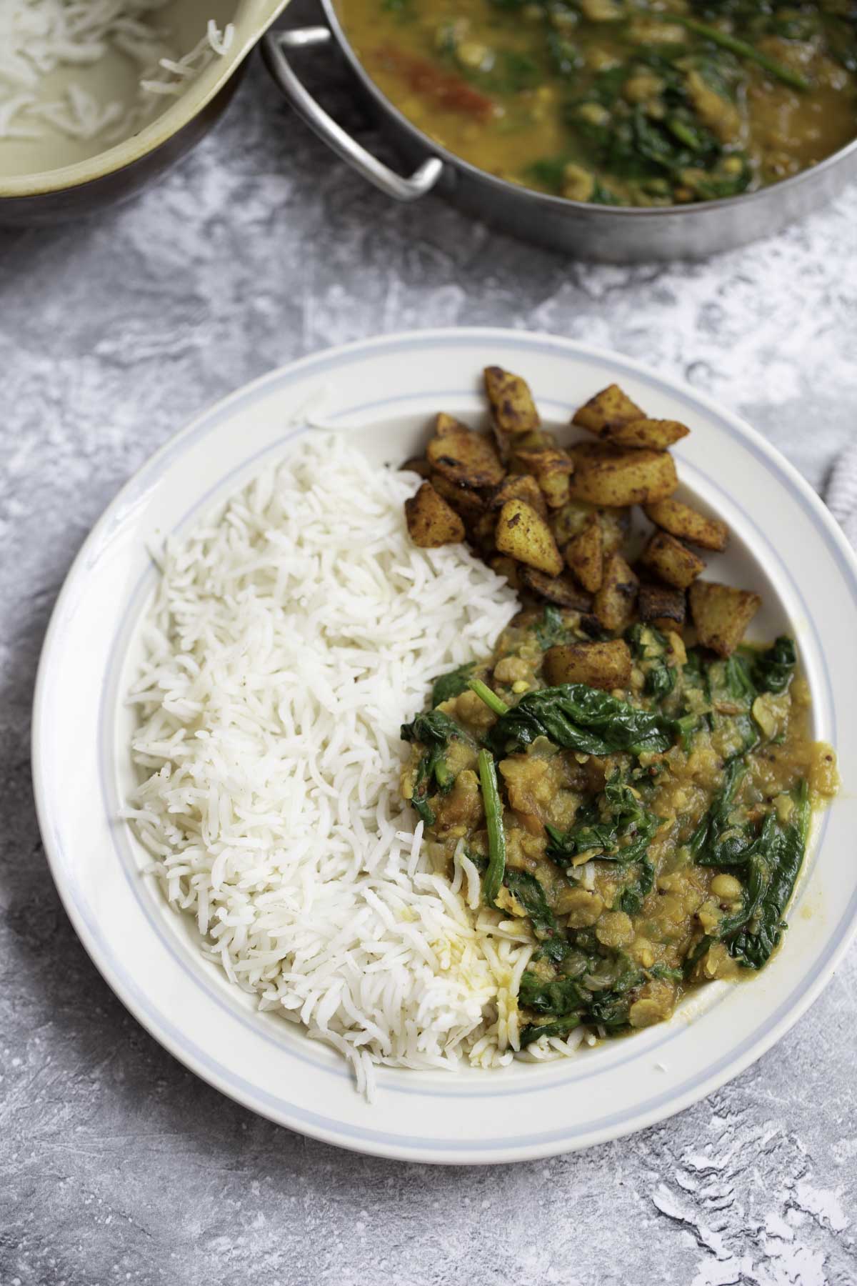 a plate of rice, spinach dal and roasted potatoes