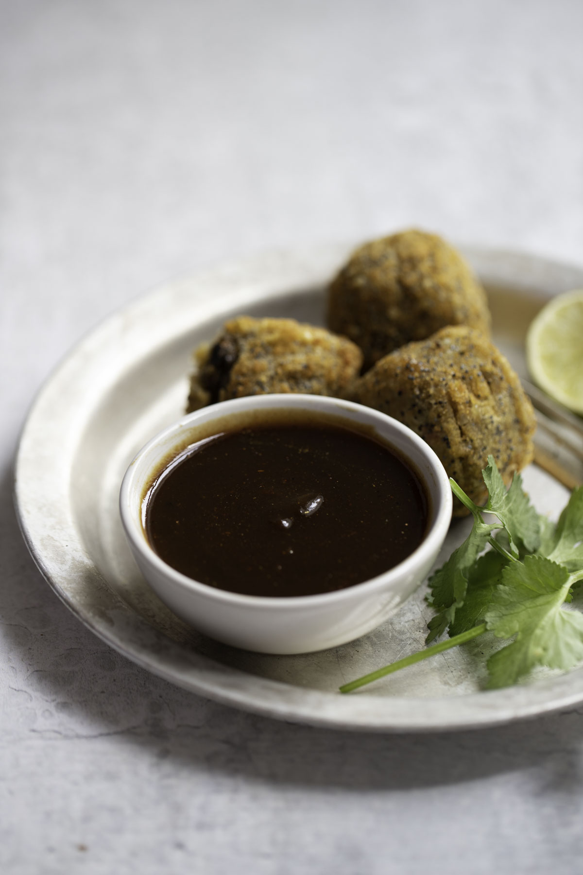 a small bowl of tamarind chutney served with paneer balls in a plate with lemon wedge