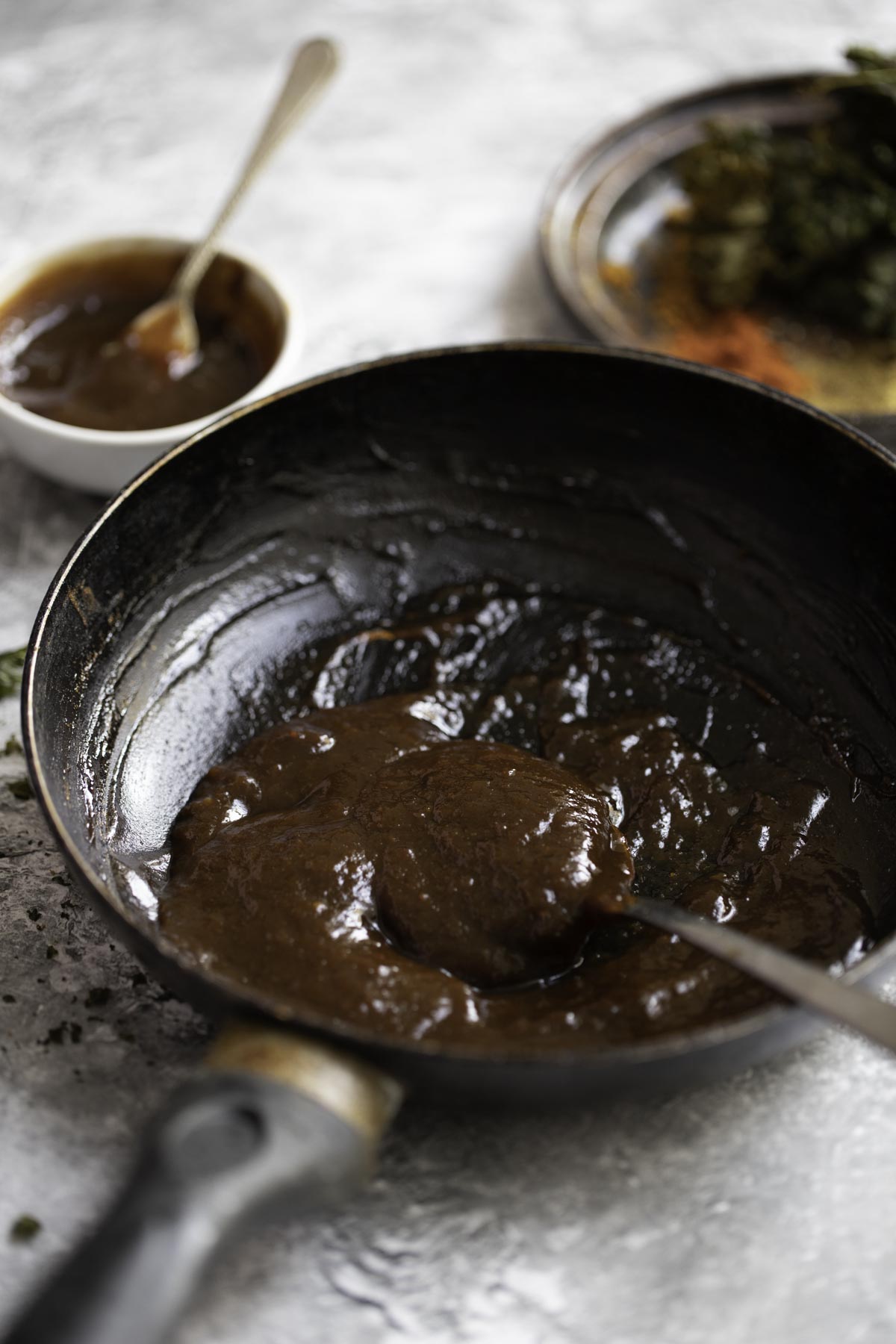 tamarind sauce in a pan, with spices and a small bowl in the background